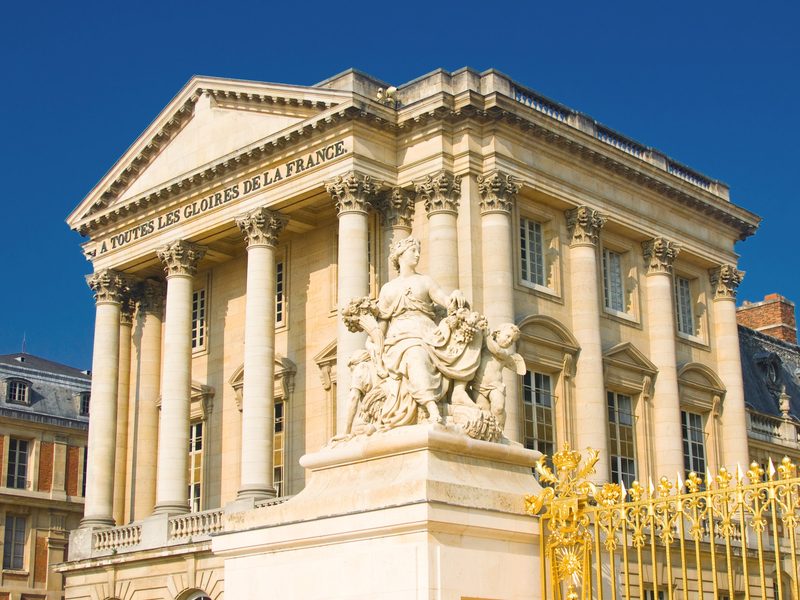 The Palace of Versailles facade and golden gate under a blue sky